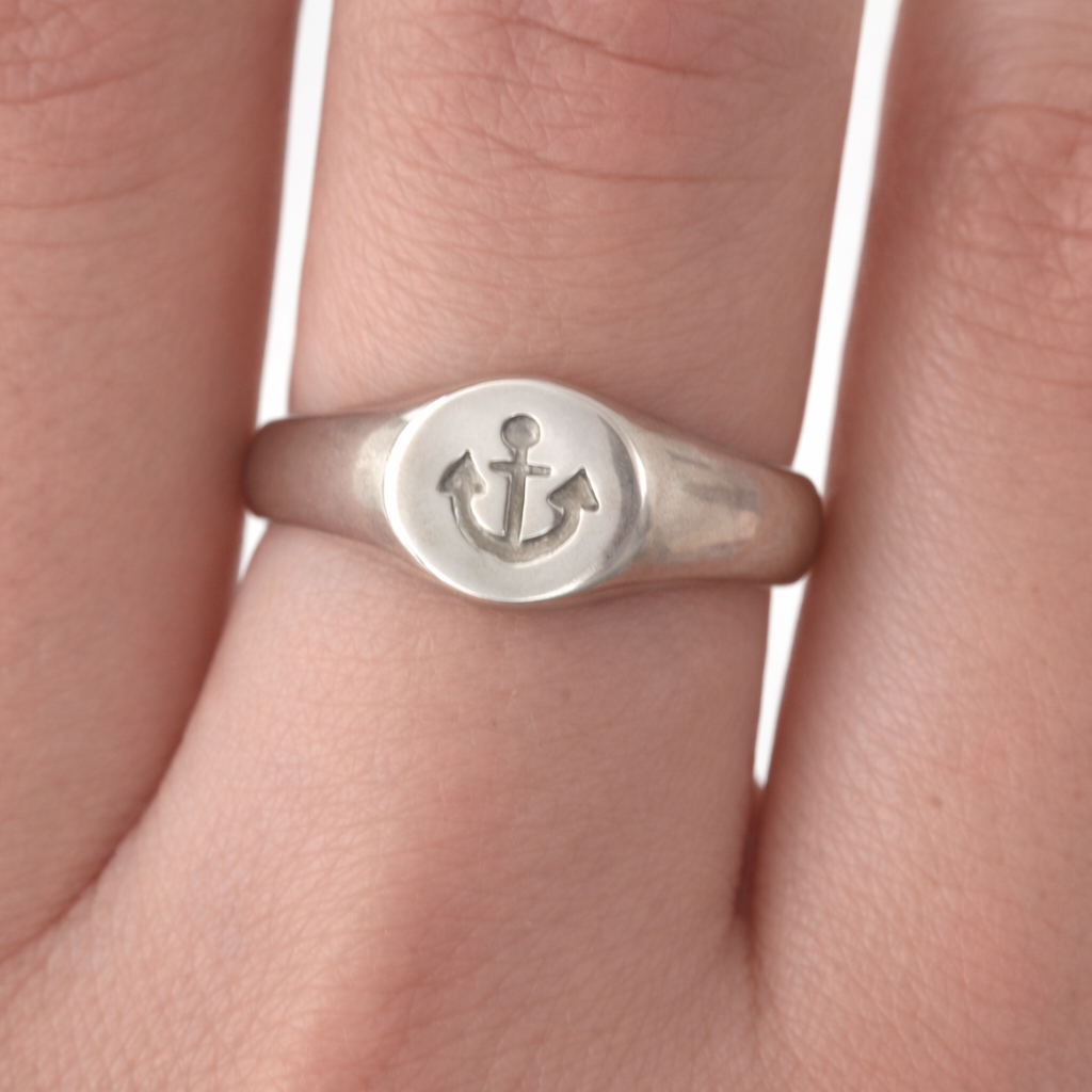 Silver ring with anchor symbol on a finger against a white background